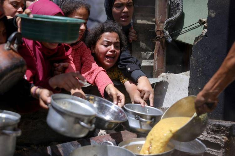 Palestinesi sfollati si riuniscono per raccogliere porzioni di cibo cotto durante una distribuzione di beneficenza a Jabalia, nel nord della Striscia di Gaza - (Afp)